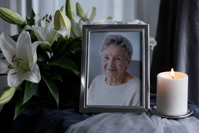 A framed photo of a smiling grandmother beside white lilies and a lit candle